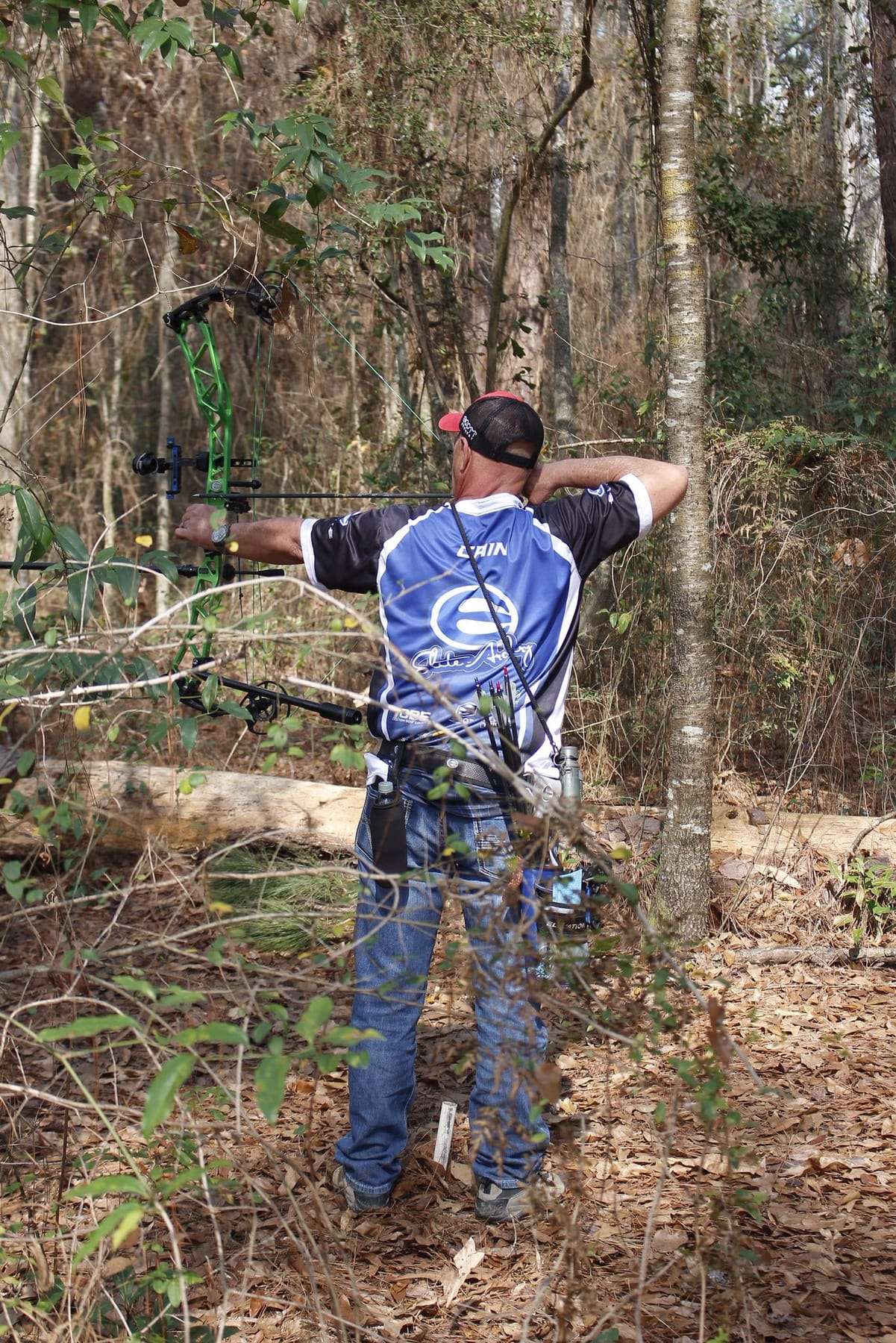 Archer at full draw with a compound bow on a wooded 3D course